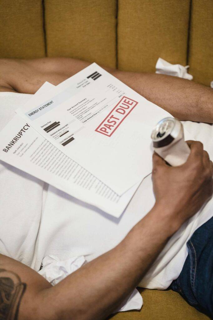 A man lying down with past due letters and bills on his chest, symbolizing the impact of bankruptcy and financial distress in the UK since 2000