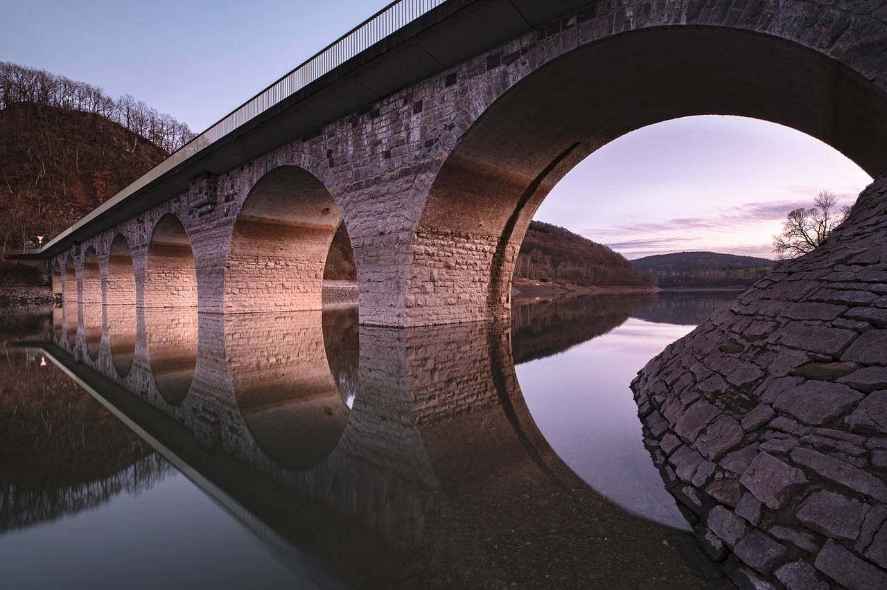 A bridge with multiple arches reflected in the water, symbolizing the concept of bridging loans and the BRRR (Buy, Rehab, Rent, Refinance) method in real estate investment