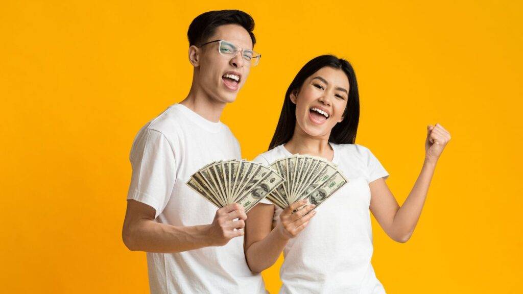 Happy couple holding cash, symbolizing the success of building and sticking to a budget effectively.