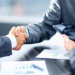 Two professionals shaking hands over a desk with financial documents, representing a comprehensive guide to personal loan jargon in the UK