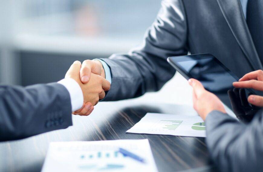 Two professionals shaking hands over a desk with financial documents, representing a comprehensive guide to personal loan jargon in the UK