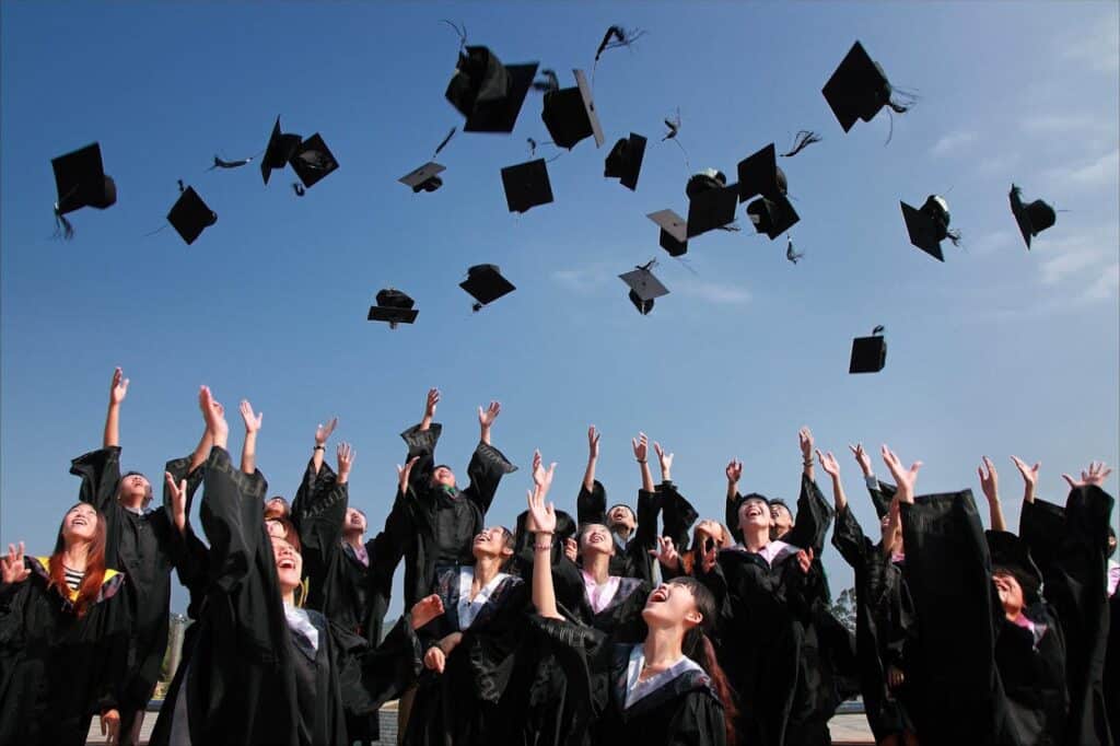 Group of graduates throwing their caps in the air, symbolizing the relationship between academic performance and real-life achievement