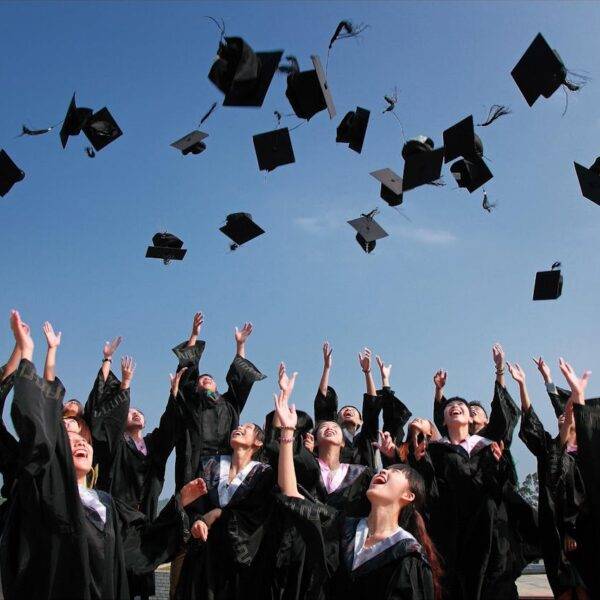 Group of graduates throwing their caps in the air, symbolizing the relationship between academic performance and real-life achievement