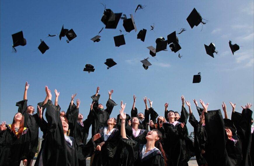 Group of graduates throwing their caps in the air, symbolizing the relationship between academic performance and real-life achievement