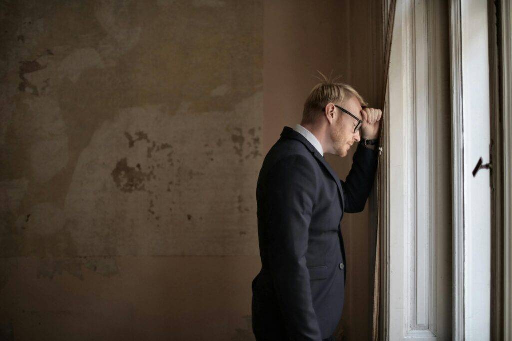 A distressed man in a suit leaning against a window, symbolizing the emotional and financial strain of filing for bankruptcy in the UK