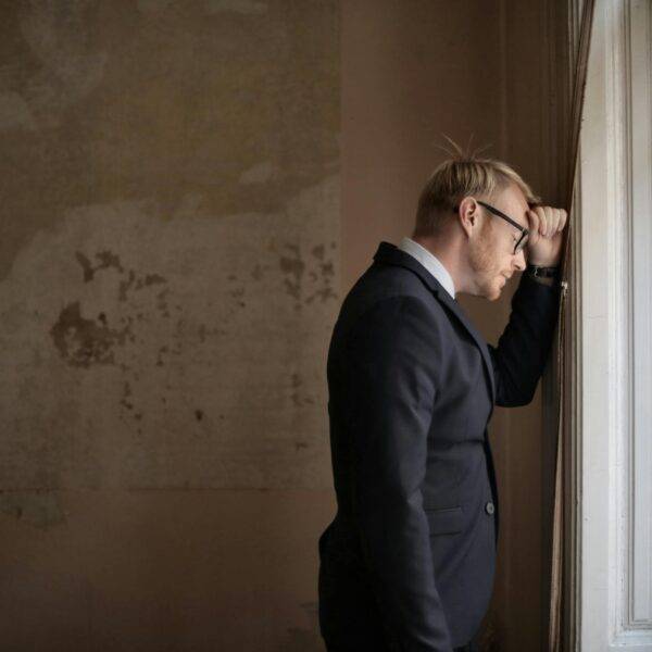 A distressed man in a suit leaning against a window, symbolizing the emotional and financial strain of filing for bankruptcy in the UK