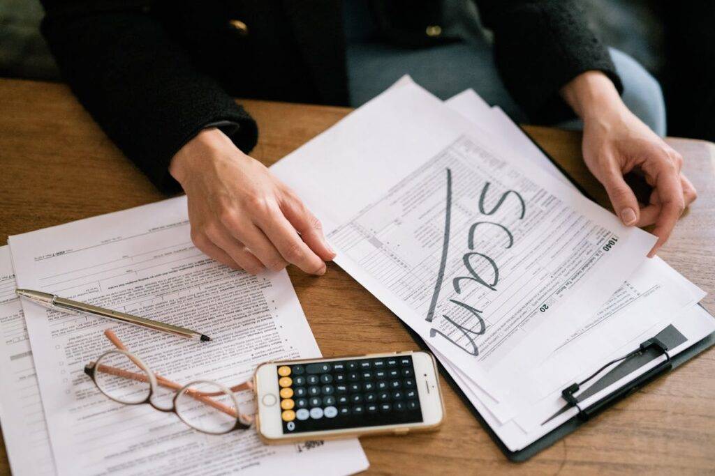 Person reviewing documents with the word "scam" written on one, highlighting the rise of online and telephone scams in the UK and their economic impact