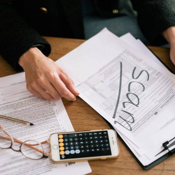 Person reviewing documents with the word "scam" written on one, highlighting the rise of online and telephone scams in the UK and their economic impact