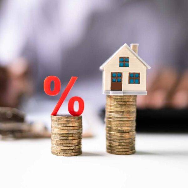 Stacked coins with a percentage symbol and a house model, illustrating the decision between remortgaging now or waiting for potential rate cuts in the UK