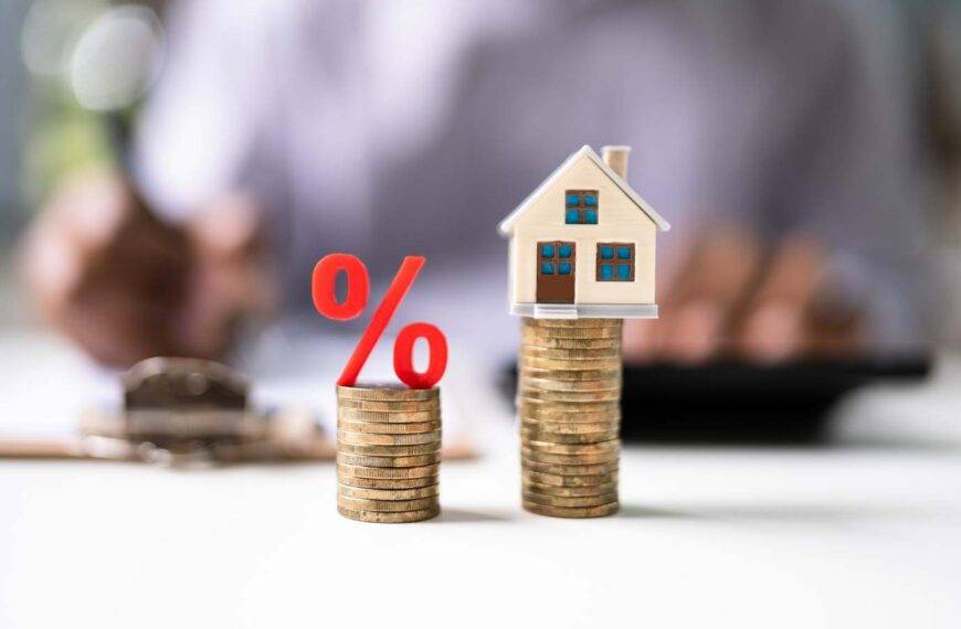 Stacked coins with a percentage symbol and a house model, illustrating the decision between remortgaging now or waiting for potential rate cuts in the UK