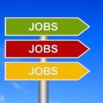 Three directional signs labeled "Jobs" in different colors against a clear blue sky, symbolizing employment challenges.