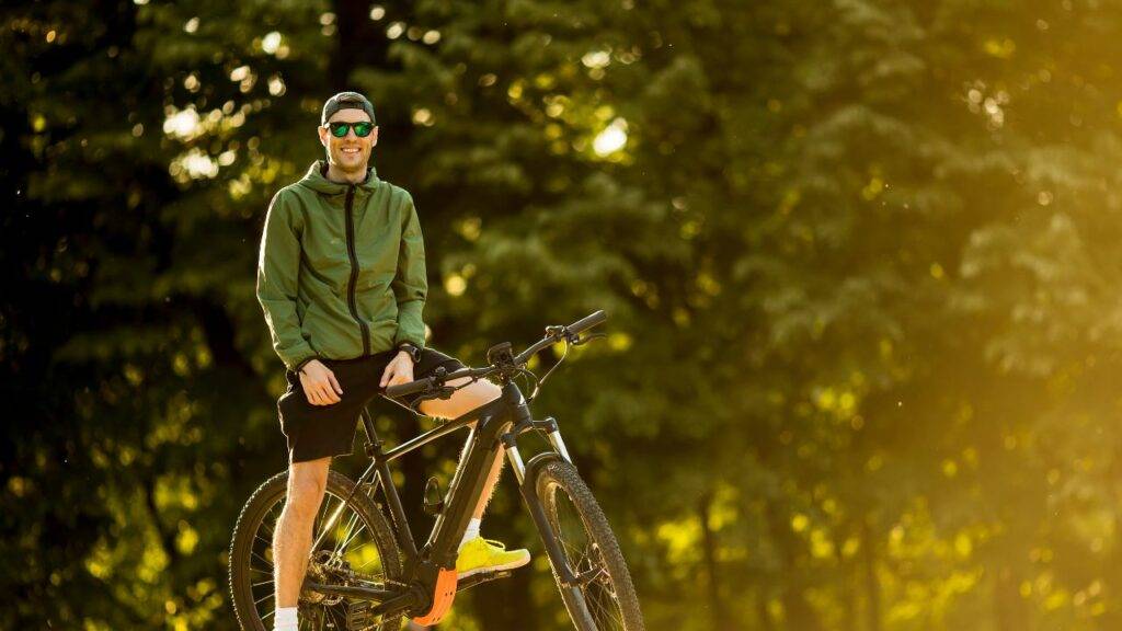 A man in outdoor gear stands with his electric bike, highlighting the importance of insuring e-bikes