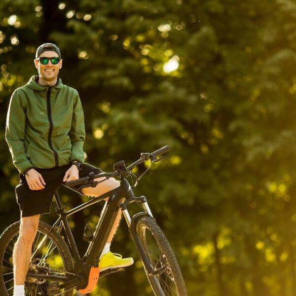 A man in outdoor gear stands with his electric bike, highlighting the importance of insuring e-bikes