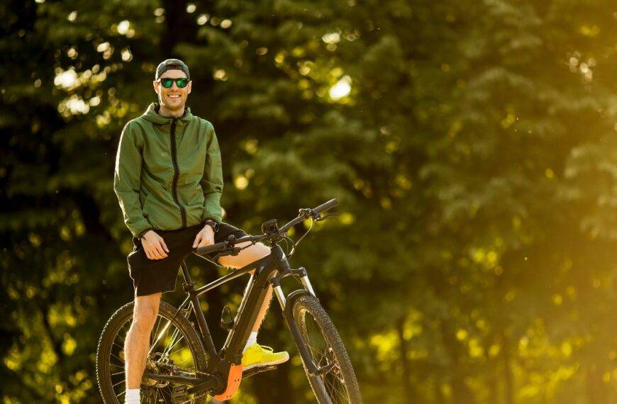 A man in outdoor gear stands with his electric bike, highlighting the importance of insuring e-bikes