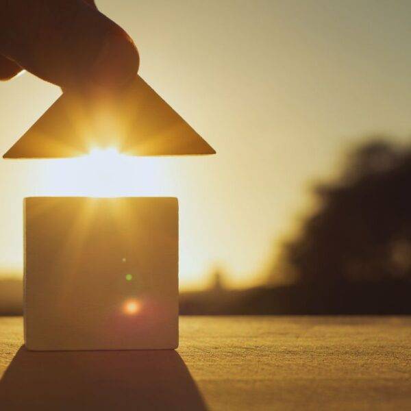 Hand placing a roof on a small house model with the sun setting in the background, symbolizing the importance of a Lady Bird Deed