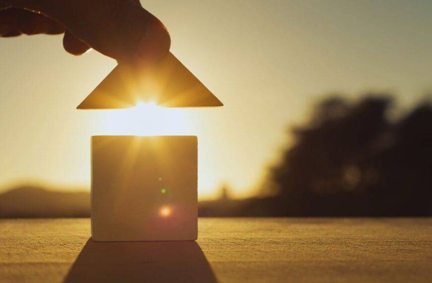 Hand placing a roof on a small house model with the sun setting in the background, symbolizing the importance of a Lady Bird Deed