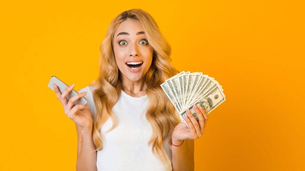 Excited woman holding cash and a phone, representing ways to make money online for beginners