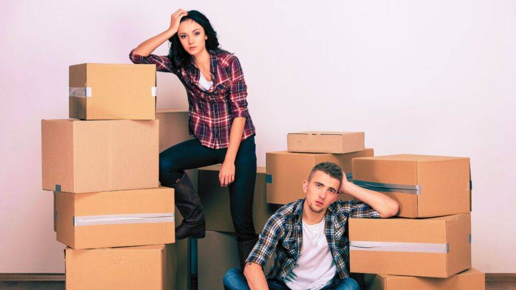 frustrated couple sitting among moving boxes, symbolizing the stress of relocation and the need for financial assistance.