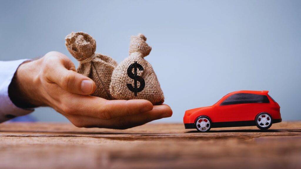 A hand holding money bags next to a red toy car, symbolizing car loan pre-approval.