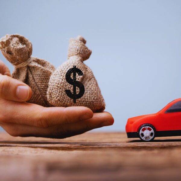 A hand holding money bags next to a red toy car, symbolizing car loan pre-approval.