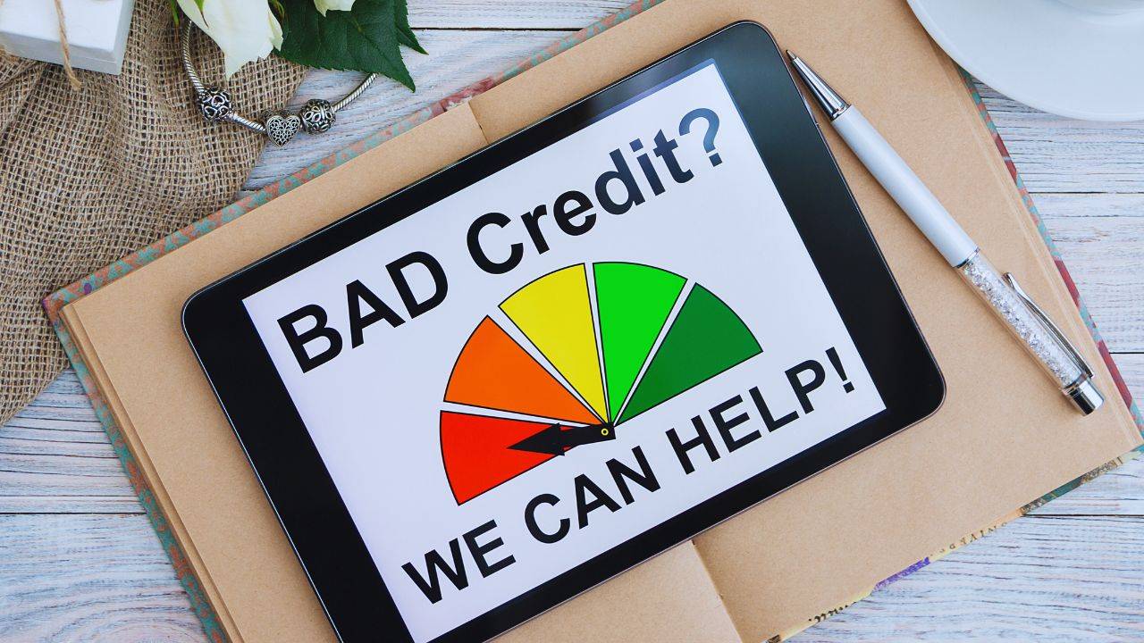 Tablet displaying a credit score gauge with the text "Bad Credit? We Can Help!" on a desk, representing credit improvement tools.