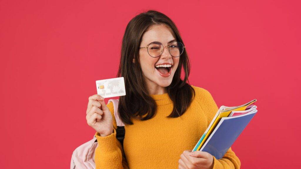 A student happily holding a credit card while carrying school supplies, highlighting the best credit card options for students