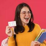 A student happily holding a credit card while carrying school supplies, highlighting the best credit card options for students